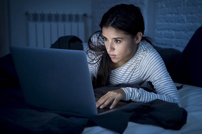 Frau surft im Bett am Laptop auf der Suche nach Cybersex